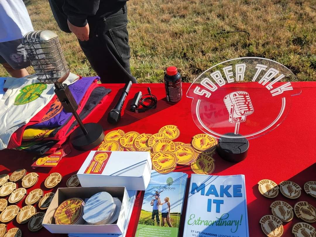SoberTalk merch table with medallions, books and the mic logo