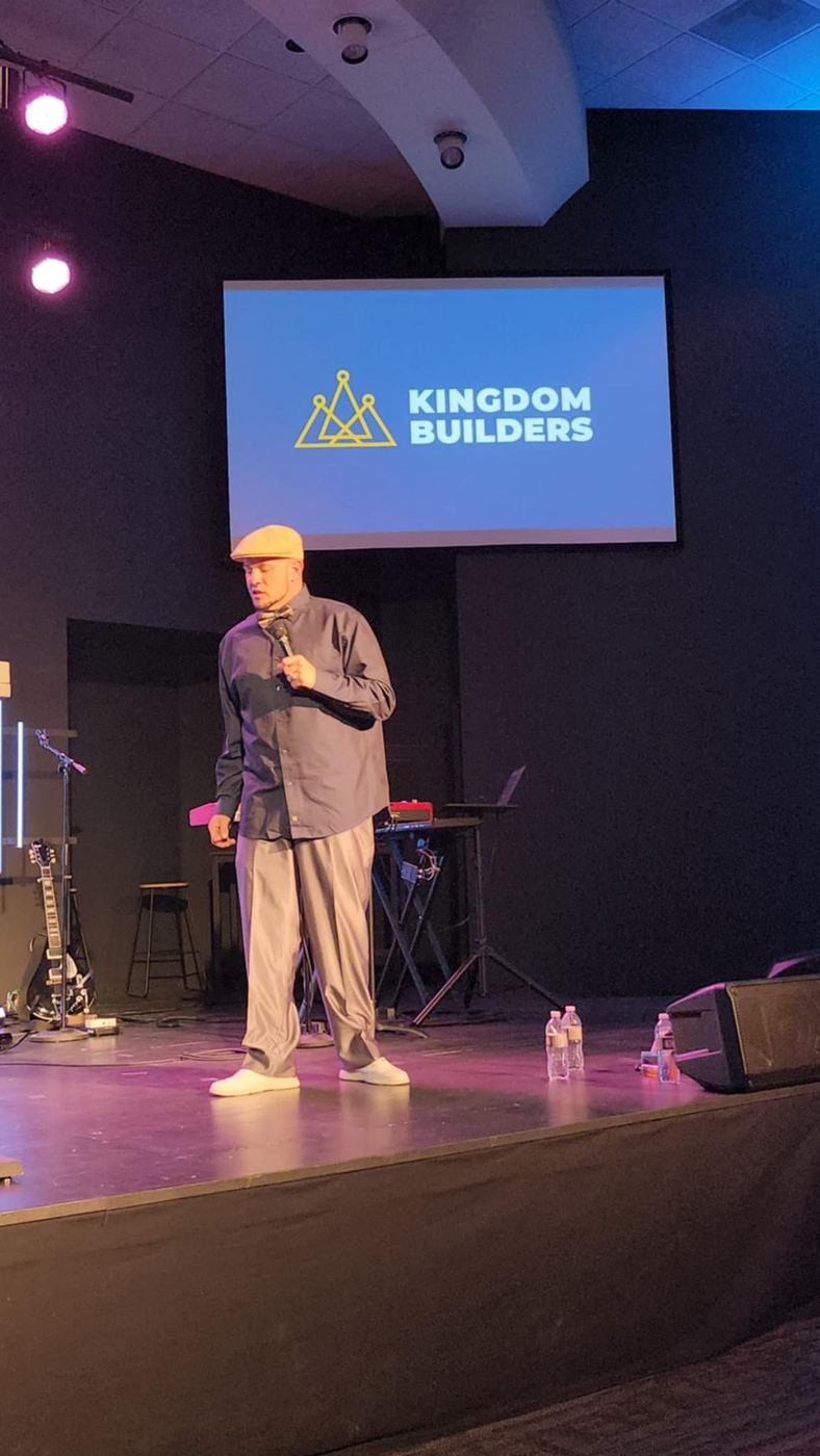 Brandon on stage with a mic in front of a Kingdom Builders screen